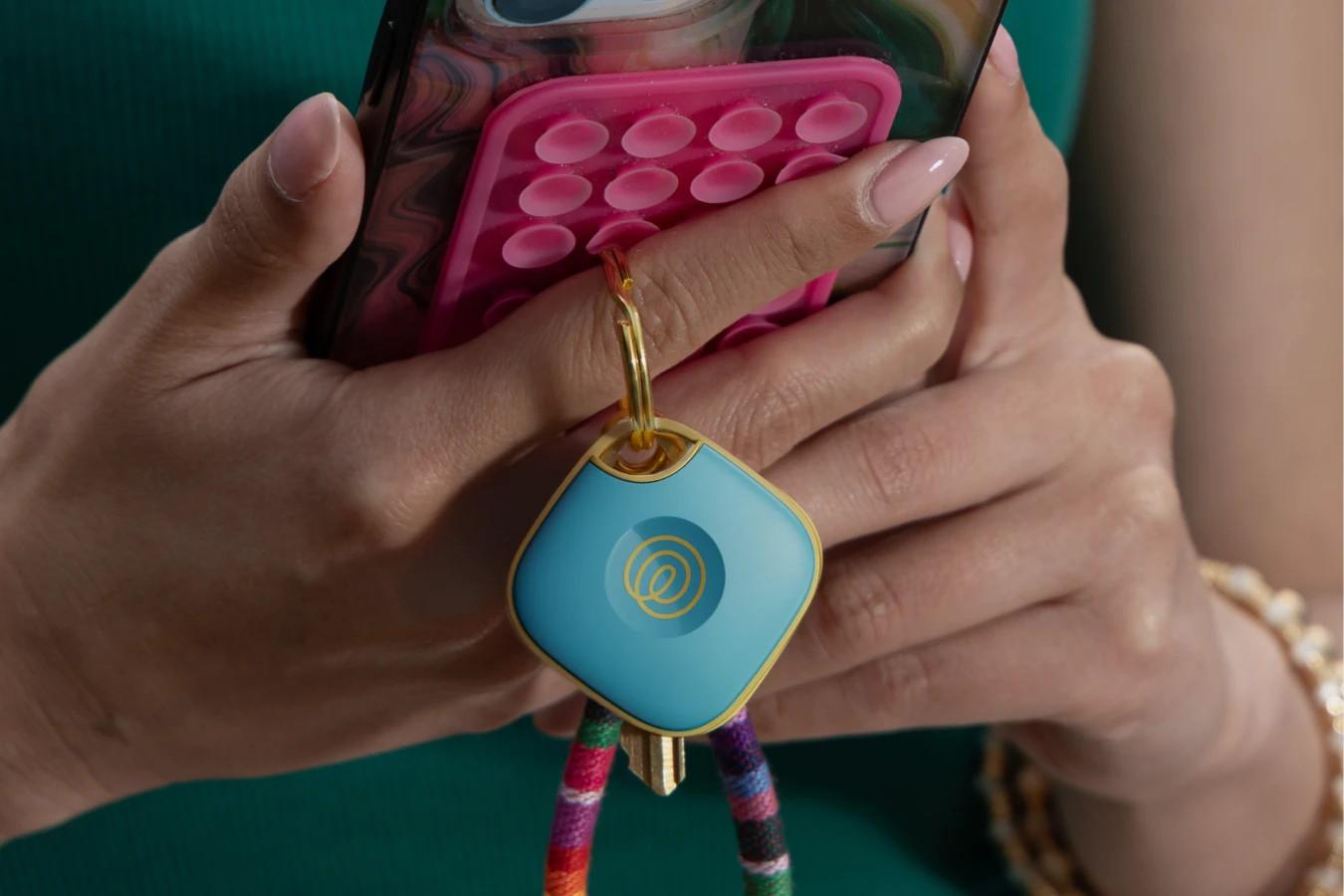 A person holding their phone and keys with a Life360 Tile - Aqua Lemon attached to it.