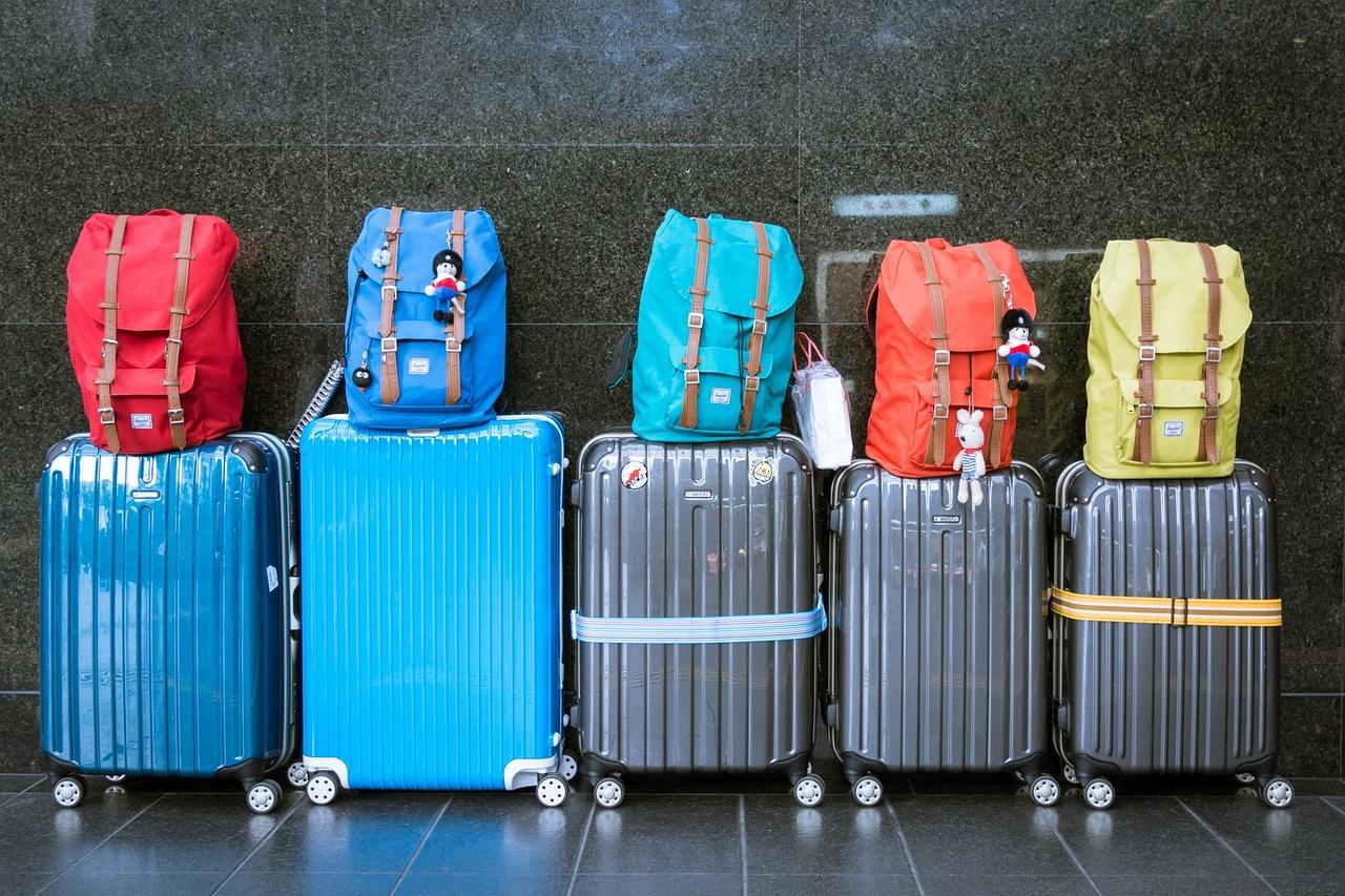 Five suitcases with backpacks on top lined up against a wall