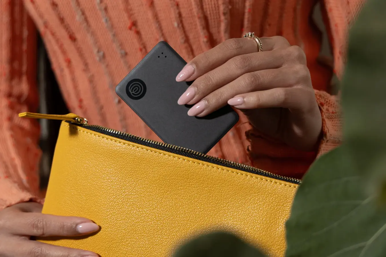 A Life360 Tile Slim being placed in a yellow pouch.