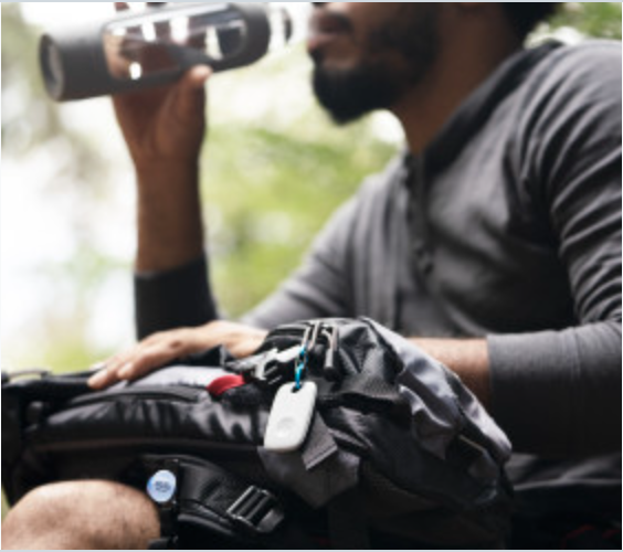 A person drinking water with a Tile pro on their backpack