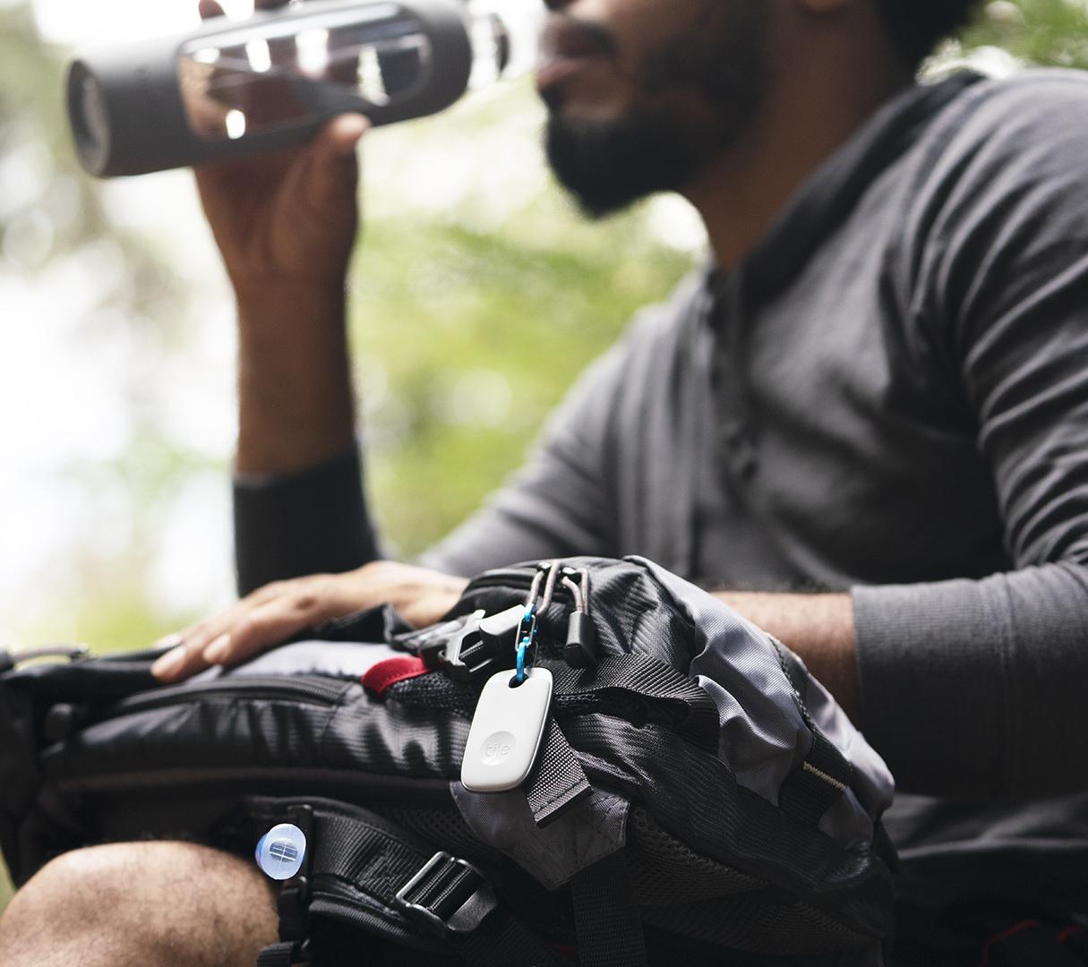 A person drinking water with a Tile pro on their backpack