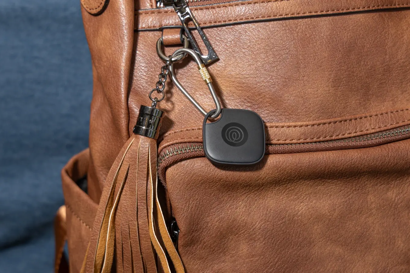A Life360 Tile attached to brown backpack.