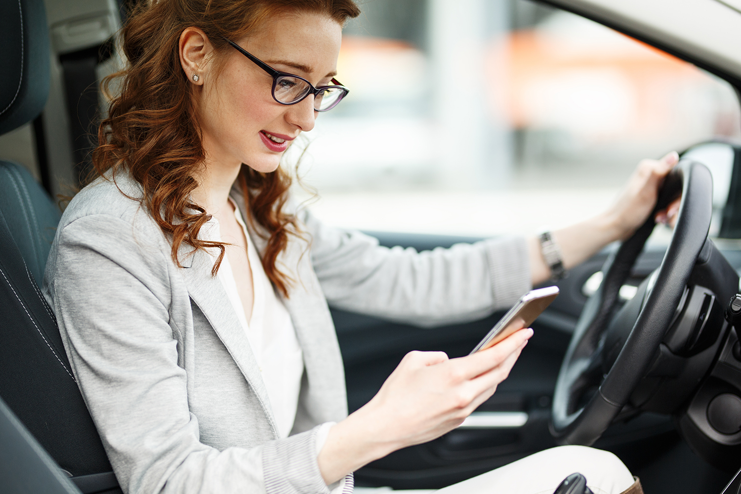 Woman wearing glasses looking down at her phone while driving