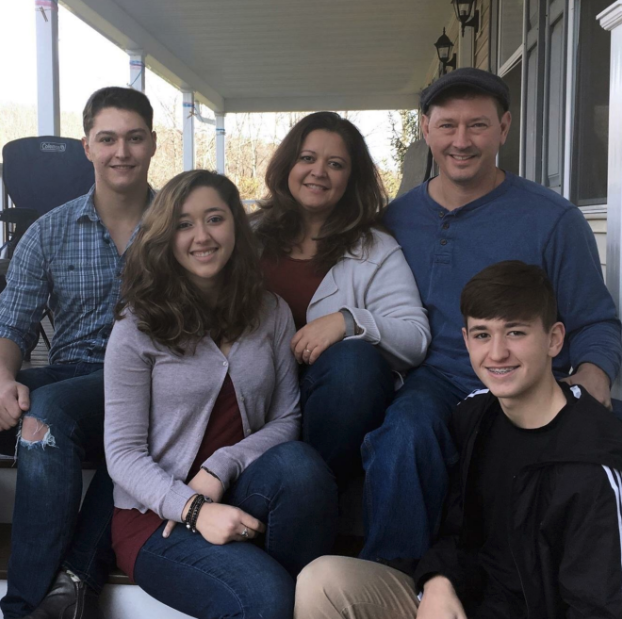 A family of 5 smiling and posing on a front porch