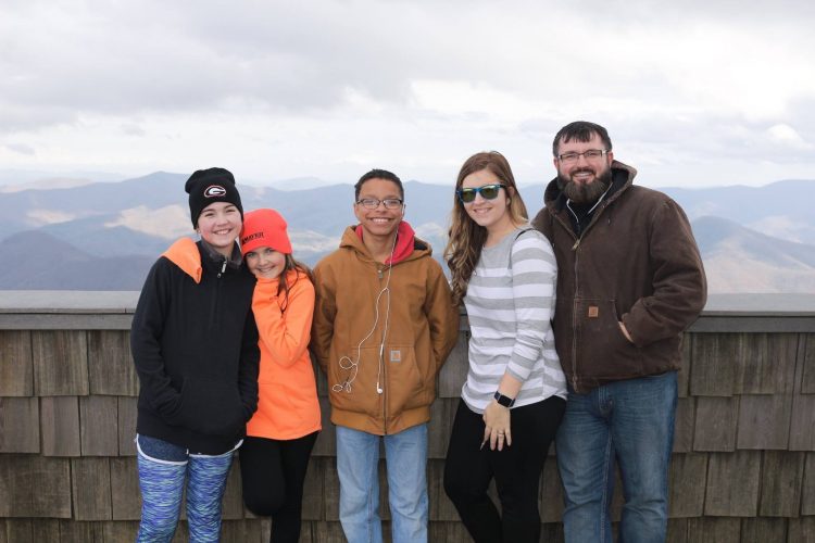 A family of 5 posing for a picture in front of a mountain range