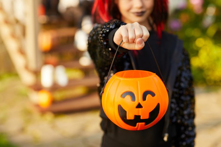 Teenage girl in a black costume holding a pumpkin trick or treat bucket