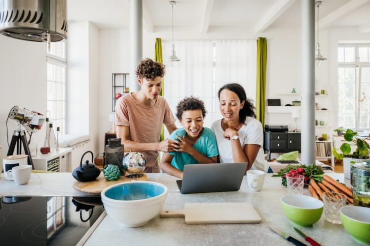 Mother and two sons in kitchen looking at a laptop together