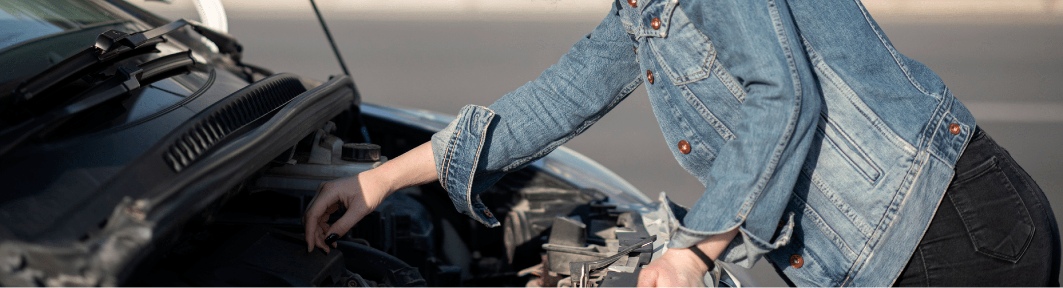 Woman in jean jacket checking engine under hood of a car