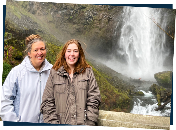 Mother and daughter standing next to each other smiling in front of a waterfall
