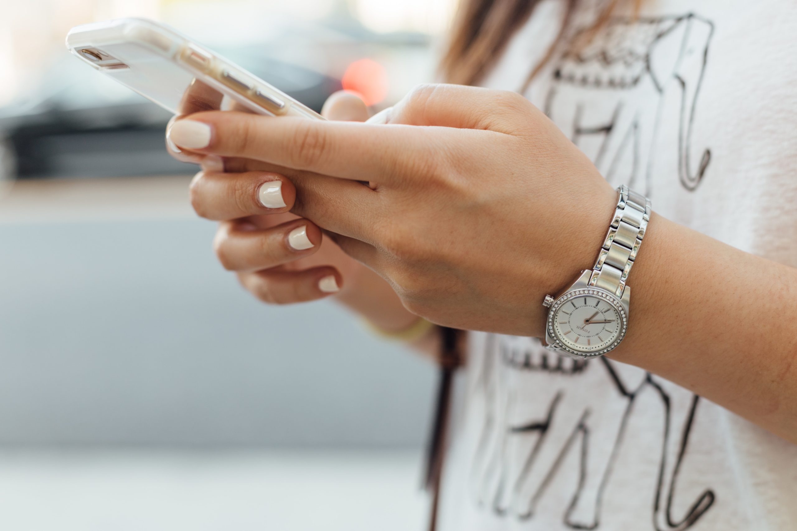 Girl with white nail polish and silver wrist watch holding a phone.