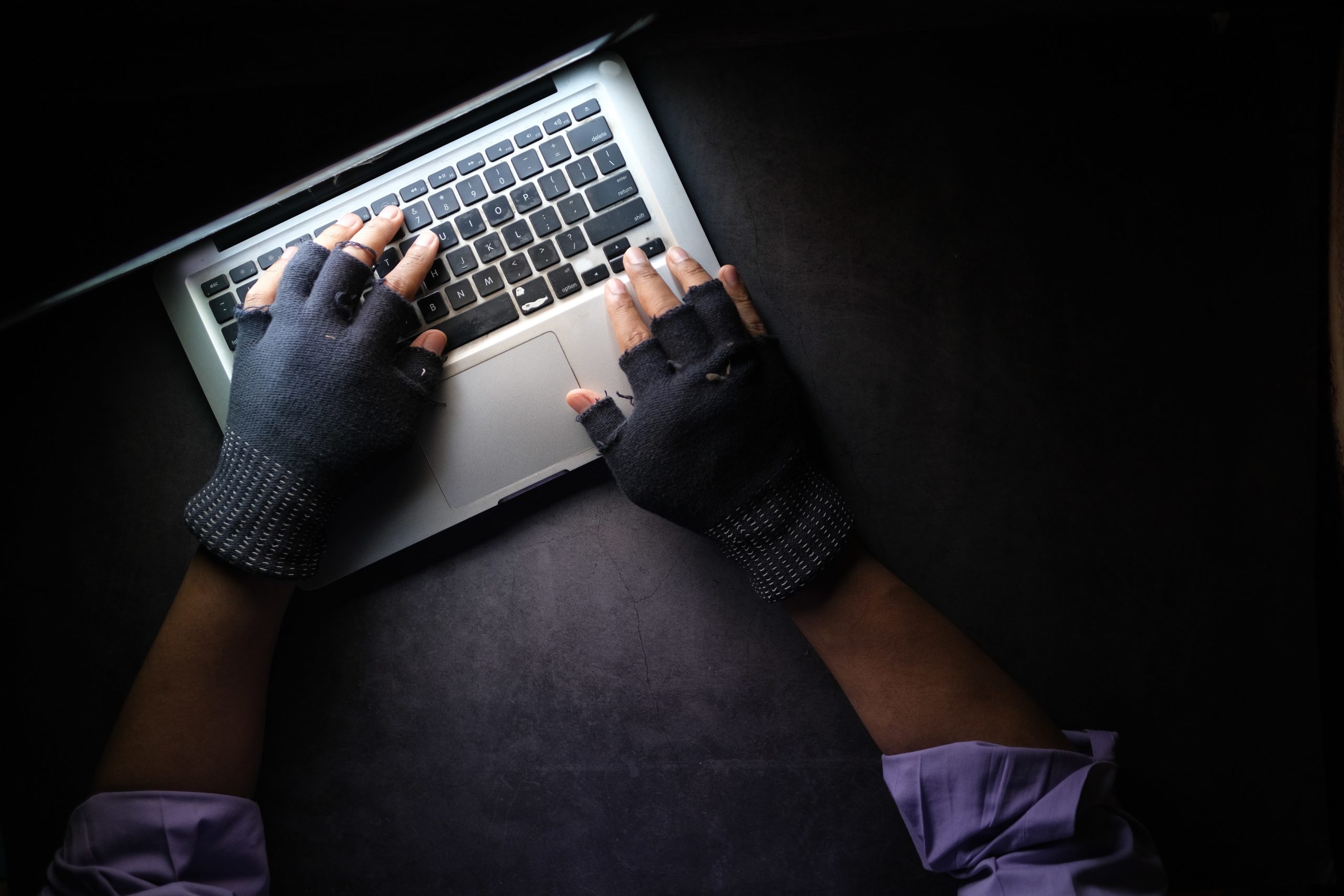 Aerial view of hands with fingerless gloves on Macbook in the dark