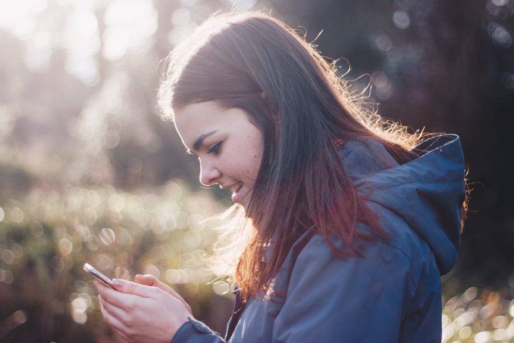 Teen girl in a hoodie smiling down at her phone