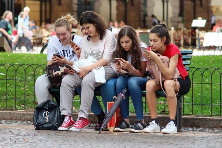 Four young girls sitting on a bench while looking at their phones