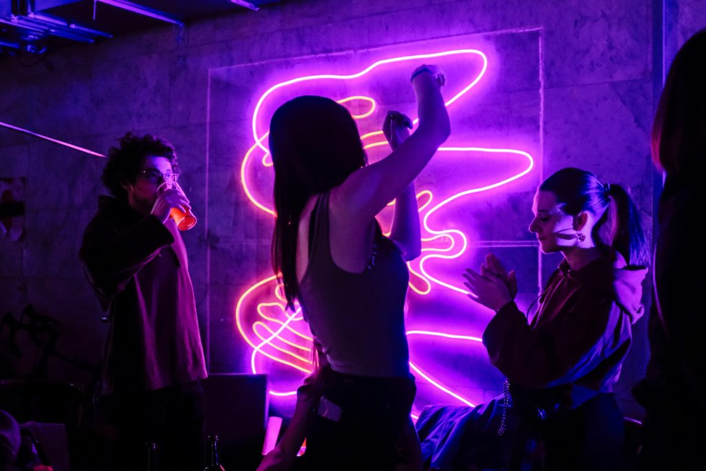 Three people dancing at a party in front of a neon light
