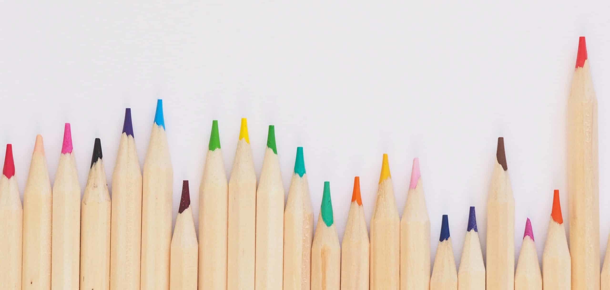 Colored pencils unevenly lined up against a white background.