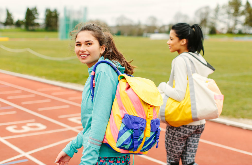 Two teen girls with backpacks walking on a school track